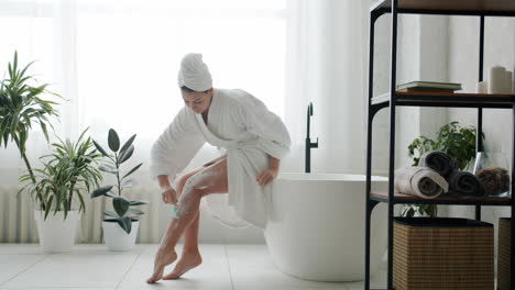 woman shaving her legs in a modern bathroom