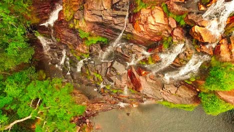 birds eye aerial shot flying up over a cliff with water streaming down