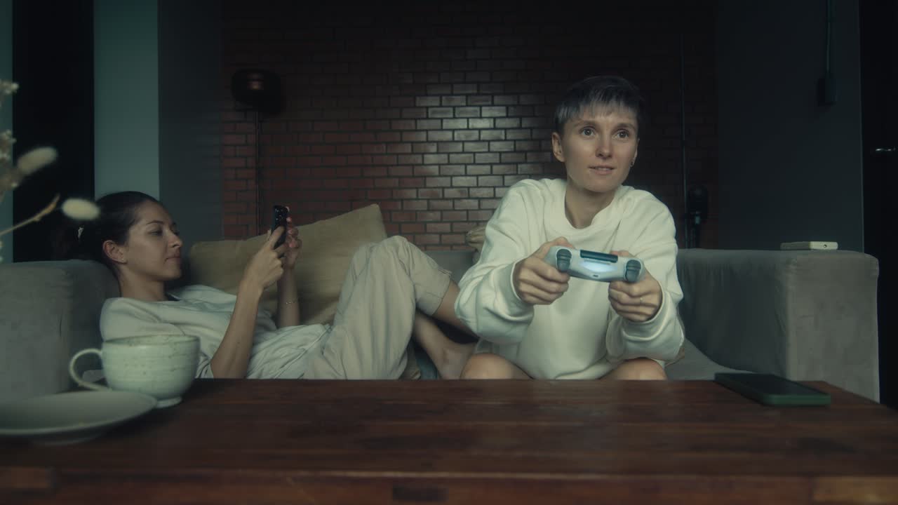 Two women playing video games on a couch at home.