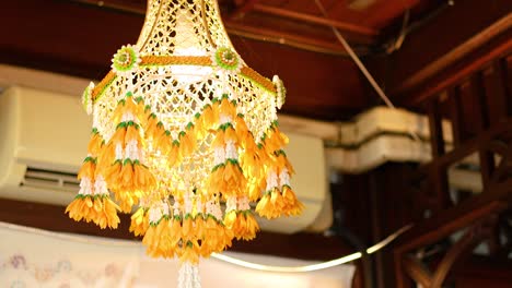 un móvil de flores tailandesa vibrante cuelga en el interior, iluminado cálidamente. el diseño intrincado y los colores brillantes crean una atmósfera festiva