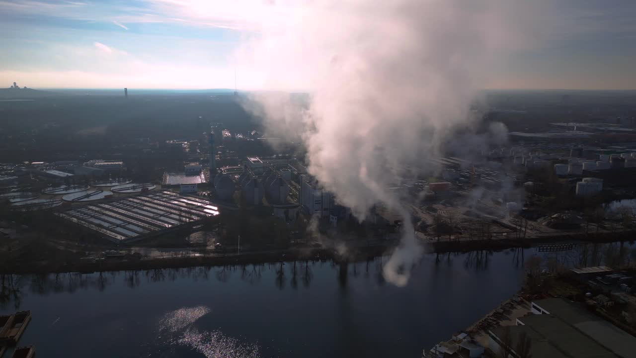 Industrial chimneys emitting white smoke over city skyline under blue sky, concept of pollution. Magic aerial view flight panorama orbit drone