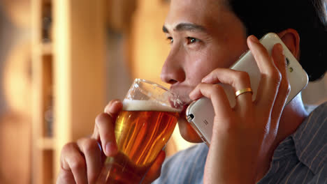 Man-having-beer-while-talking-on-mobile-phone-in-a-restaurant-4k