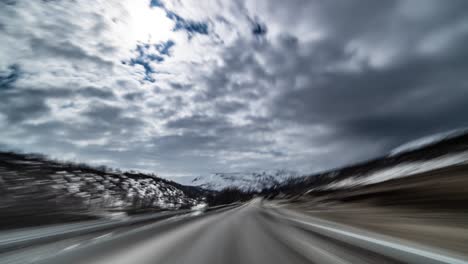 a drive on the e6 highway thought the saltfjellet mountains, crossing the arctic circle. the black stripe of the road stretches up to the horizon. snow on the ground. heavy clouds hanging above