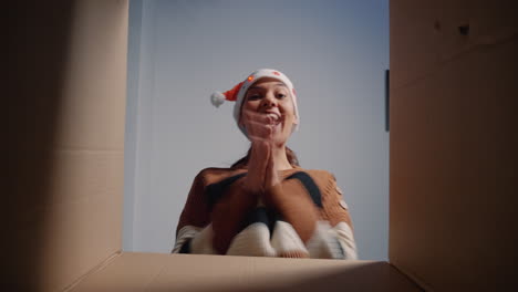 mujer caucásica con sombrero de santa abriendo una caja de regalos