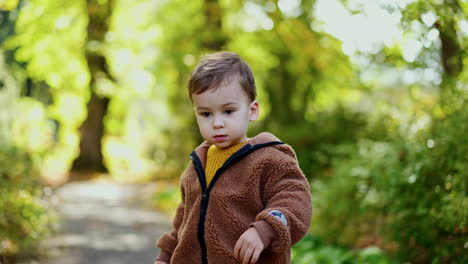 sweet little caucasian kid playing outdoors. toddler throws chestnut and run to get it. blurred nature at backdrop.