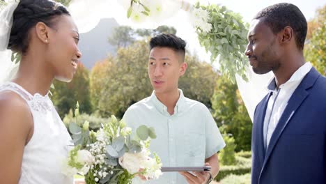 Hombre-Birracial-Oficiando-El-Matrimonio-De-Una-Feliz-Pareja-Afroamericana-En-Un-Jardín-Soleado,-En-Cámara-Lenta