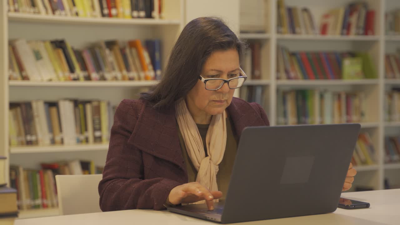 anciana concentrada en una biblioteca usando una laptop