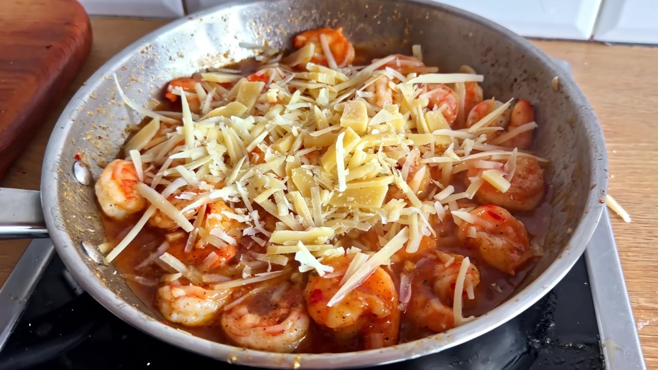 Primo piano di pasta con gamberi condita con formaggio grattugiato in una padella.