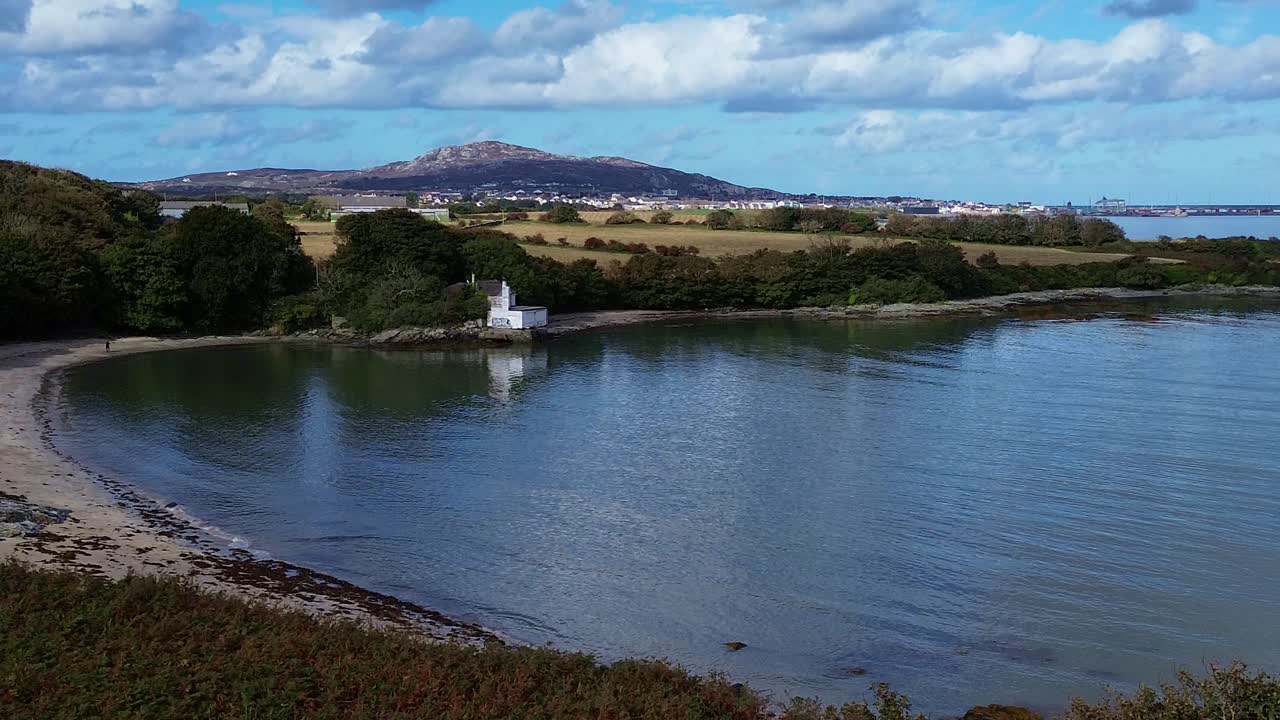 Aerial view towards Welsh crescent bay under idyllic Holyhead mountain and distant woodland farmland