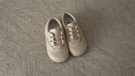 small beige baby shoes resting softly on patterned neutral fabric
