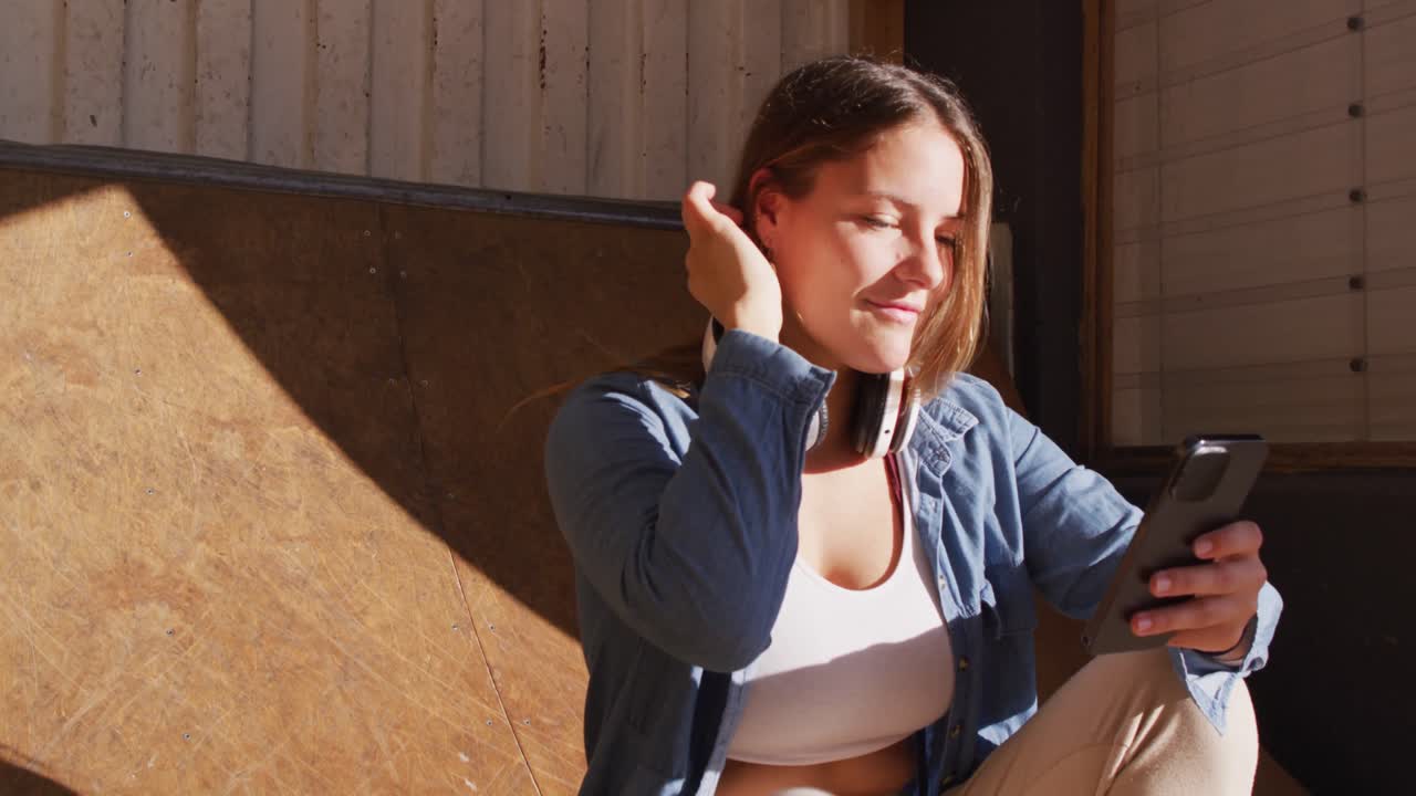 행복한 백인 여성 스케이트보더가 휴식을 취하고 스마트폰을 사용하는 비디오