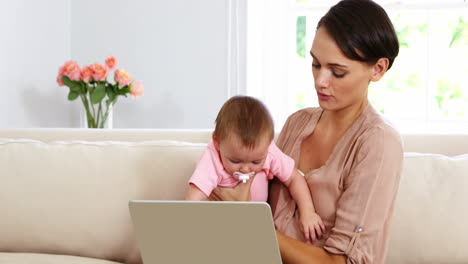 madre linda sosteniendo a su bebé y usando una computadora portátil