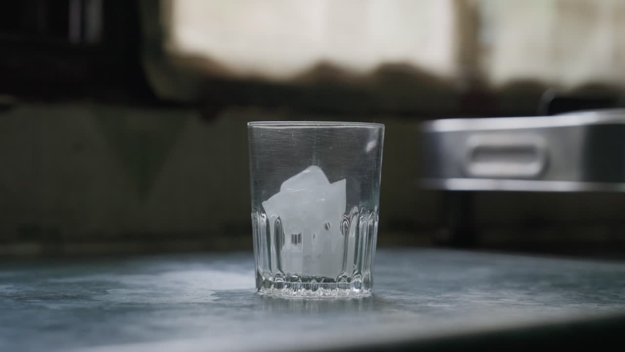 A slow-motion of a hand putting ice cubes into a glass cup against a blurred background