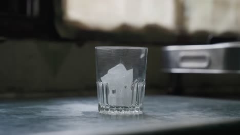 a slow-motion of a hand putting ice cubes into a glass cup against a blurred background