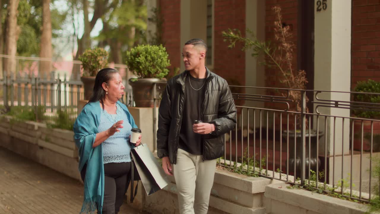 Two people walking and talking on a street while holding coffee and shopping bags