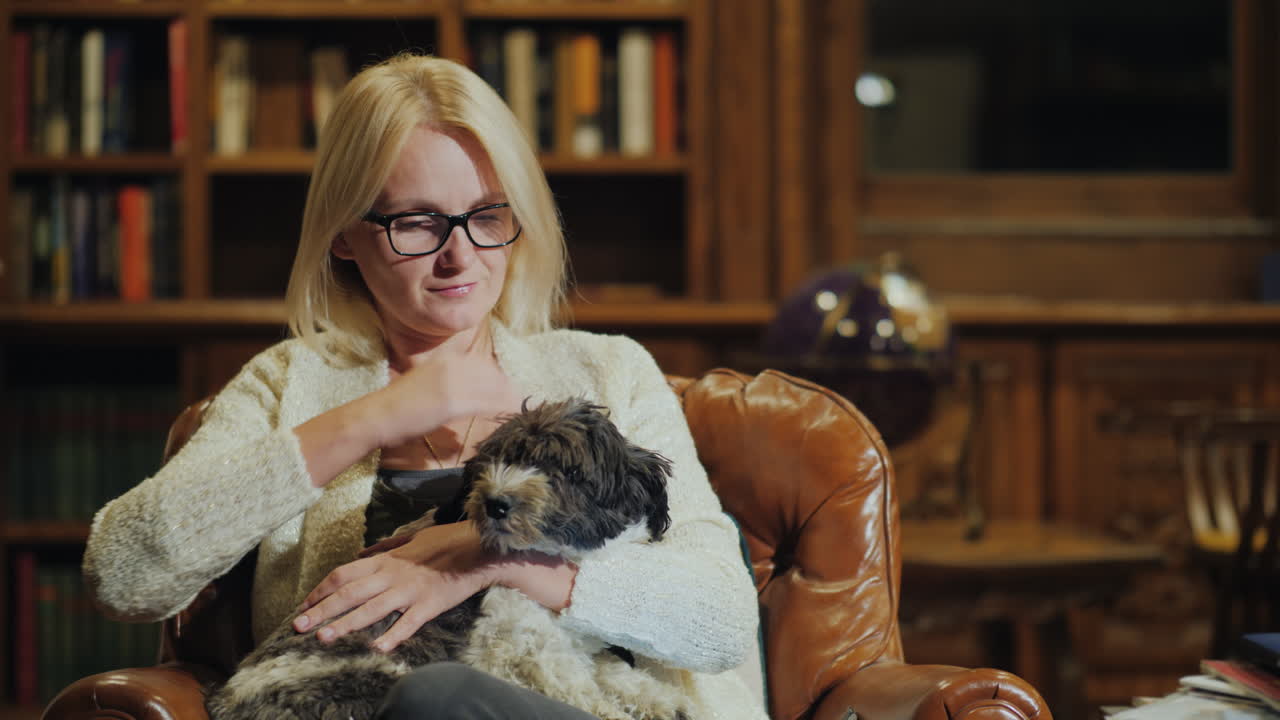 한 여성이 고급스러운 홈 라이브러리에서 작은 개를 안고 휴식을 취하고 있습니다.