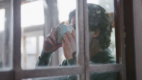 Hombre-Caucásico-Tomando-Café-Y-Mirando-Por-La-Ventana-En-Casa,-Cámara-Lenta