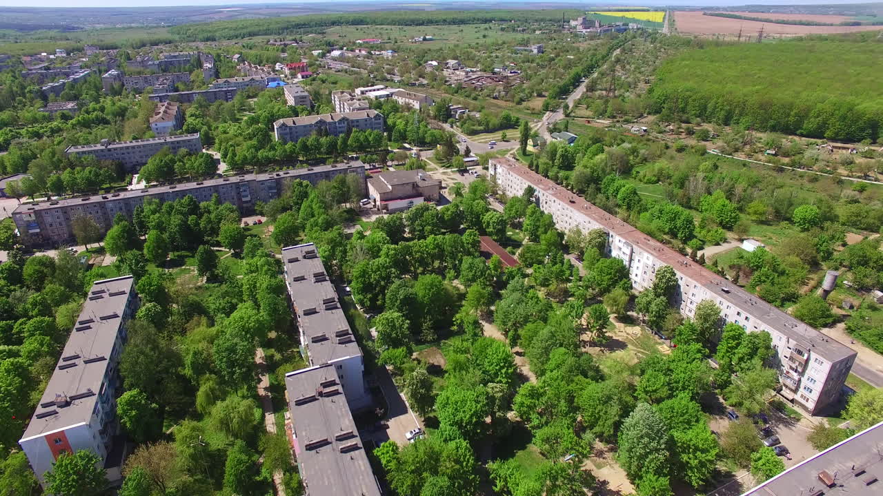 Long multi-storied buildings in the residential area of a green city on summer day. Agricultural fields at backdrop. Aerial view.