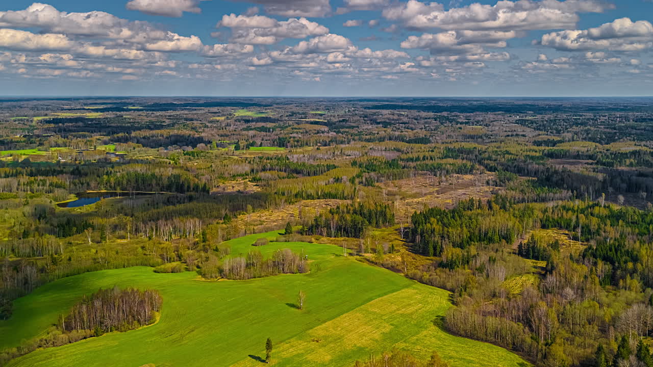 Farms, crops, meadows, fields, forests, and ponds in a rural landscape under a dreamy cloudscape time lapse as seen from high altitude