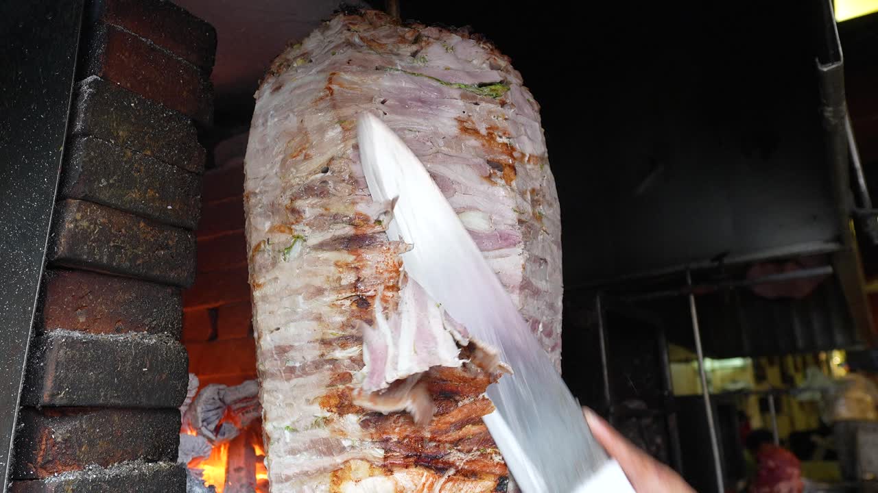 Al pastor meat being sliced directly from vertical spit