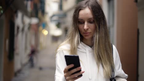 mujer rubia caminando por la vieja calle usando un teléfono inteligente