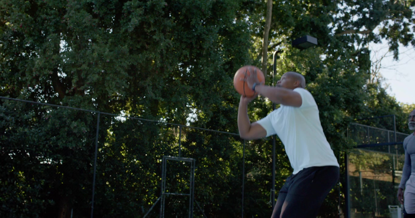 Diverse men on court, pink hoodie man dribbling, passing ball, teammate shooting at hoop to score