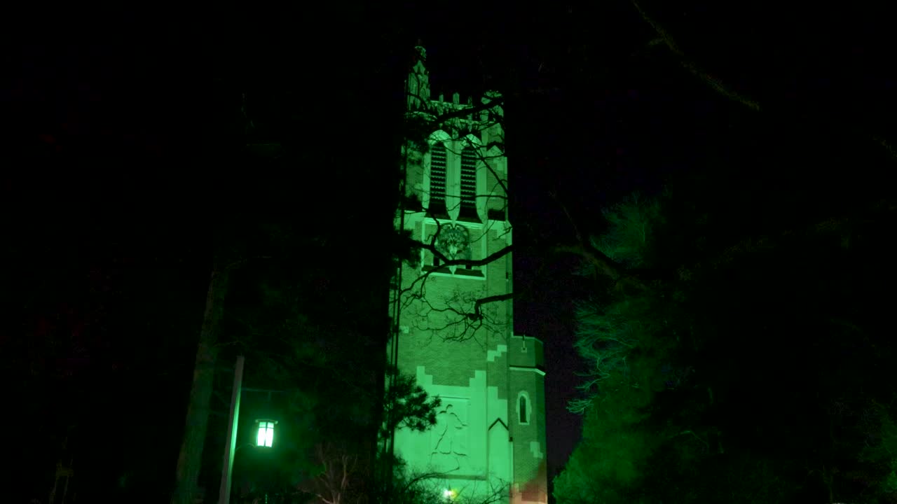 torre beaumont en el campus de la universidad estatal de michigan iluminada de noche en verde en honor a las víctimas del tiroteo masivo de febrero de 2023 con un video cardán caminando por los árboles hacia adelante