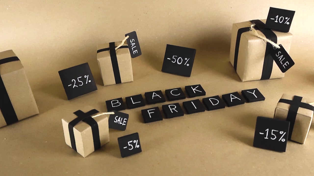 Handmade craft paper gift boxes and Black Friday lettering surrounded by discount percentages signs on a brown background, representing the annual retail sales event and consumerism