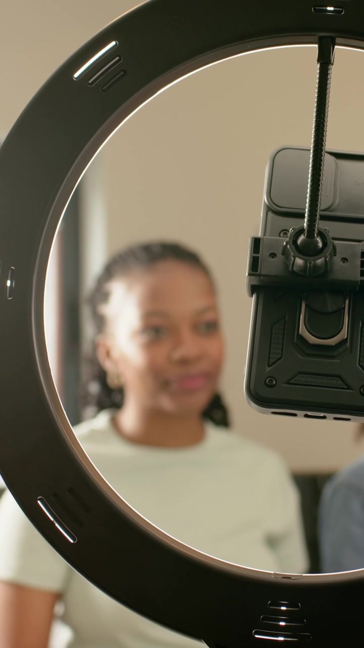 Vertical video: Smiling woman in tee checking mounted phone at home preparing shoot with ringlight