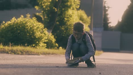 schoolboy in glasses collects books and sheets on road