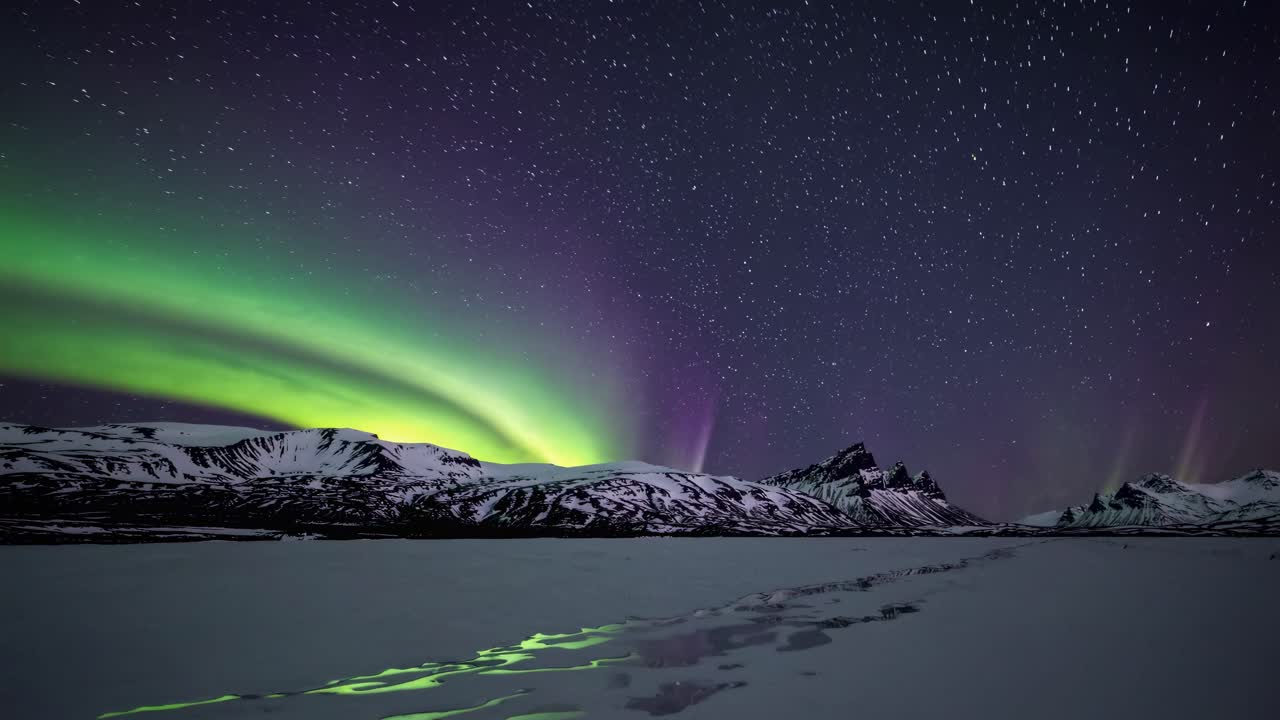 A wide-angle video captures the ethereal Northern Lights over snow-capped mountains and a frozen