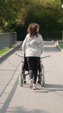 mother runs on sidewalk in city park pushing child with disability in wheelchair. happy woman and kid enjoy sunny spring day on fresh air backside view