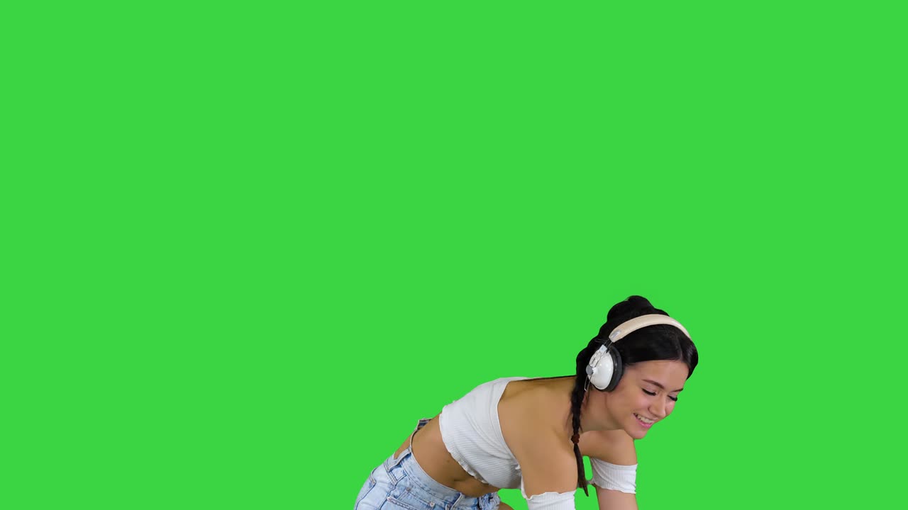 Modella caucasica con le cuffie che salta, esprimendo emozioni felici mentre ascolta musica su schermo verde, Chroma Key