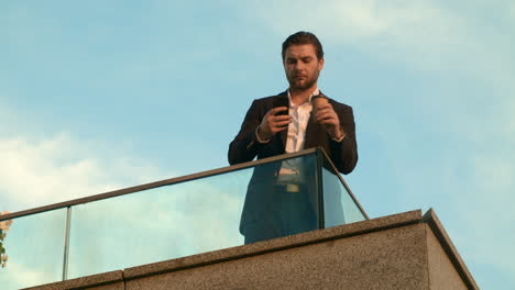 businessman using smartphone in city. manager standing on balcony with coffee