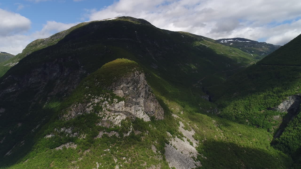 vista aérea de montañas escarpadas y amplios valles cubiertos de densa vegetación verde, afloramientos rocosos y manchas de luz solar bajo un cielo parcialmente nublado.