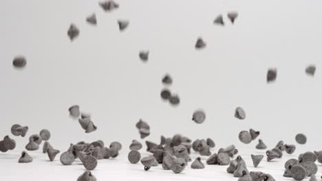 semi sweet chocolate chips falling and bouncing into pile on white table top in slow motion