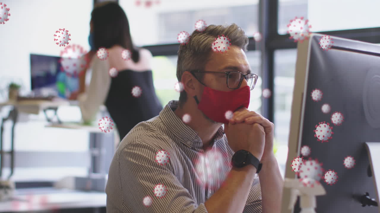 사무실에서 컴퓨터를 사용하여 얼굴 마스크를 입은 남자를 떠다니는 코로나19 세포의 애니메이션