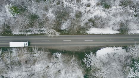 tracking a lorry from above which is driving along a straight wintry road, framed with trees from a conifer forest