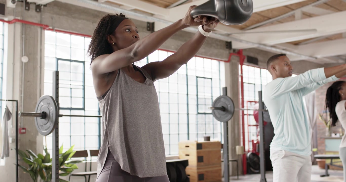 Group fitness class starting with African American woman lifting kettlebell, hinging, powering hips