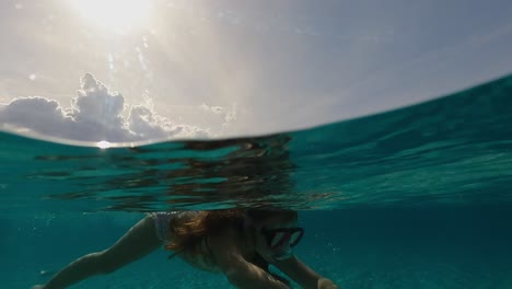 Cute-little-girl-with-long-red-hair-swimming-underwater-in-crystal-clear-ocean-water