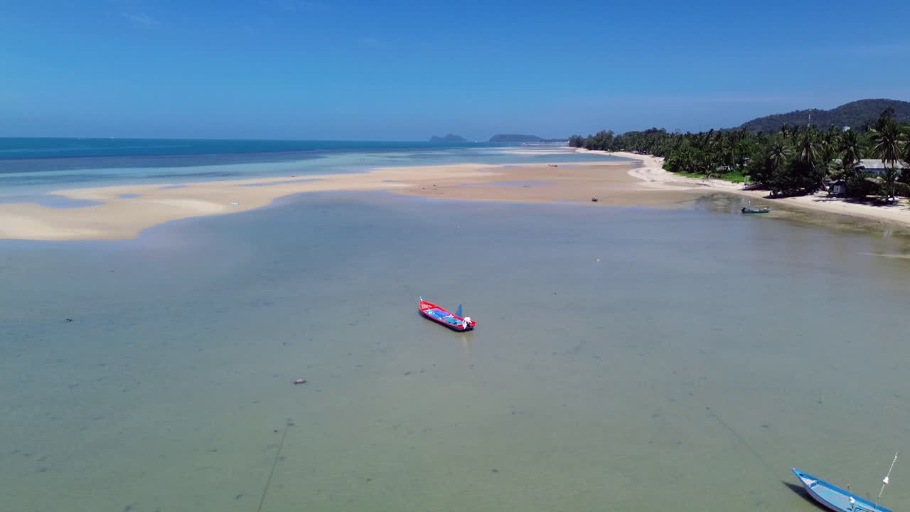Stunning drone footage captures traditional Thai fishing boats resting on the clear, shallow waters off Koh Phangan island in Thailand. A serene tropical landscape island scenery