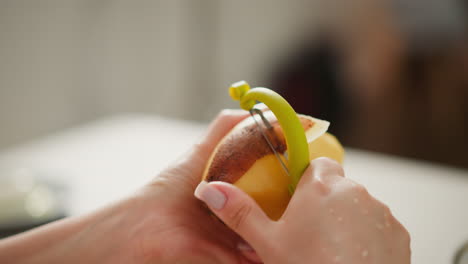 close up of person with polished nails using green peeler to remove skin from raw potato, smooth hand movement captured with blurred neutral background