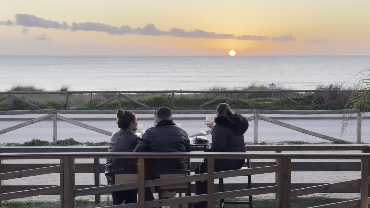 Three tourists enjoying the sunset at a cityside cafe near the ocean