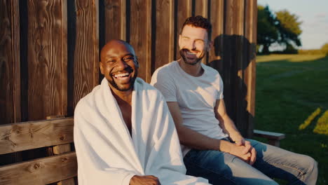 two happy men laughing together on a wooden bench outdoors