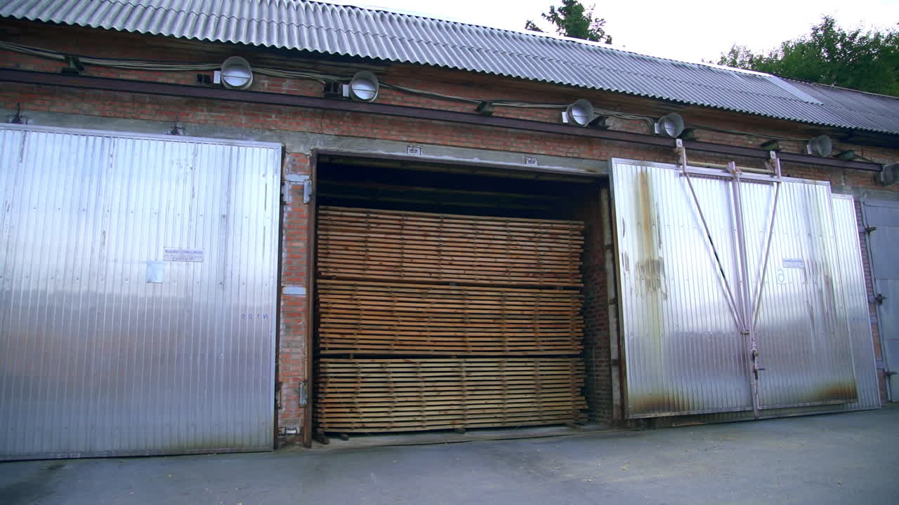 Long brick warehouse with huge metal doors. The storehouse filled with wood piled in big stacks.