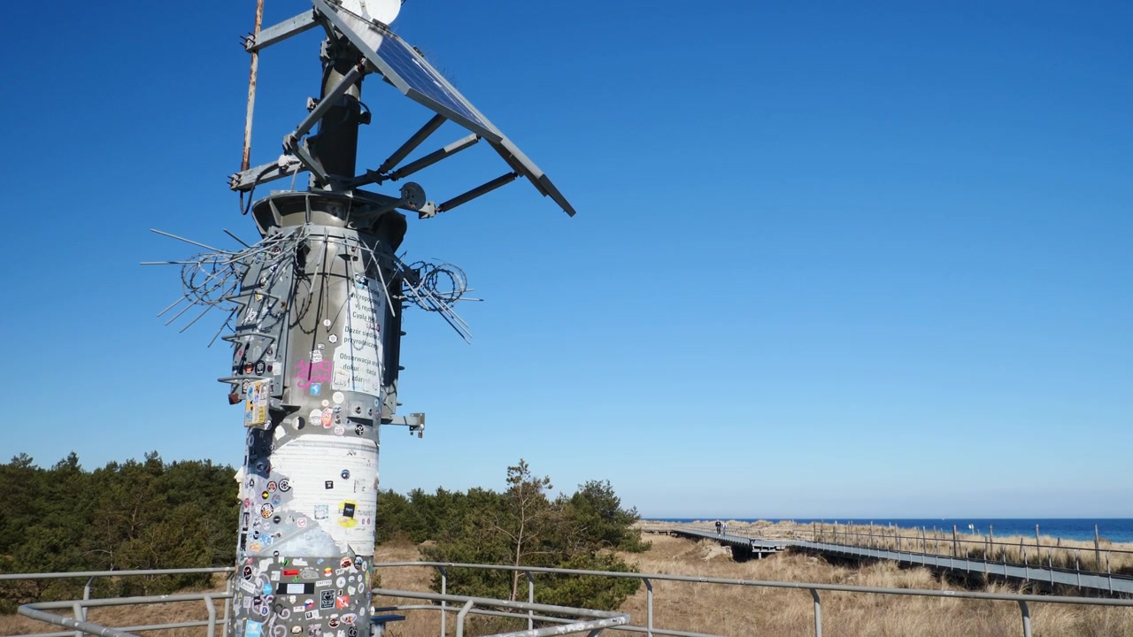 Footpath stroll along the scenic Hel Peninsula promenade in Poland, showcasing the prominent metal observation and meteorological mast towering over coastal dunes and the Baltic beach.