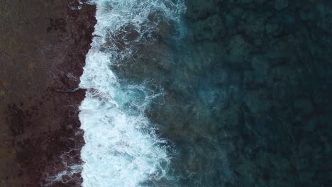 aerial: top down shot of stormy waves crashing on reefs and coastline, slow motion