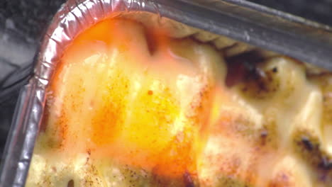 Delicious-and-tasty-authentic-and-traditional-chicken-mentai-cooking-with-red,-orange-and-yellow-hot-burner-flame-of-fire-sizzling-surface-of-food-in-silver-foil-take-out-pan,-static-extreme-close-up