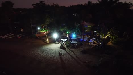 Bar-En-La-Playa-Junto-Al-Mar-Al-Atardecer-Luces-De-Colores-Disparadas-Con-Drones