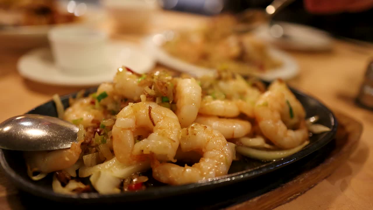 Steaming prawns with vegetables served on a hot plate in a warmly lit Asian restaurant, captured with shallow depth of field and minimal camera movement